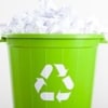 Green recycling bin with a white recycling symbol, filled with paper.